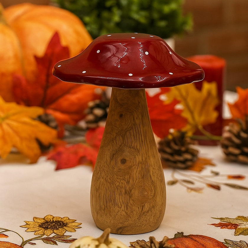 Ciupercă decorativă din lemn cu pălărie roșie așezată pe o masă decorată de toamnă
