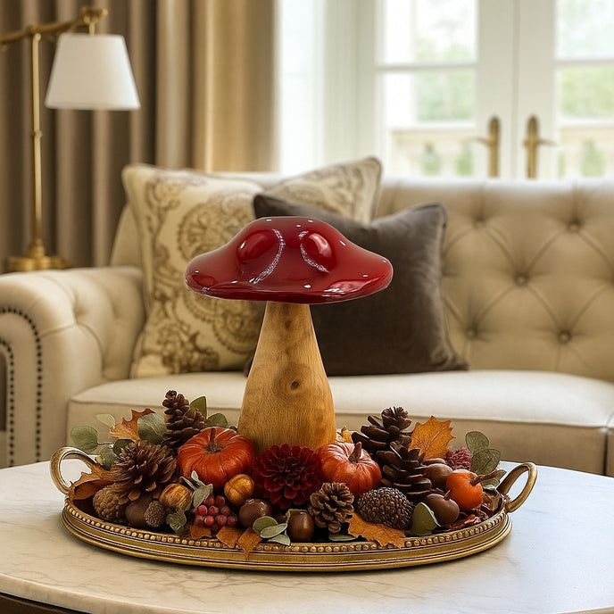 Ciupercă decorativă din lemn cu pălărie roșie așezată pe o tavă de bronz, decorată de toamnă. Tava se află pe o măsuță cu blat de marmură, în fața unei canapele