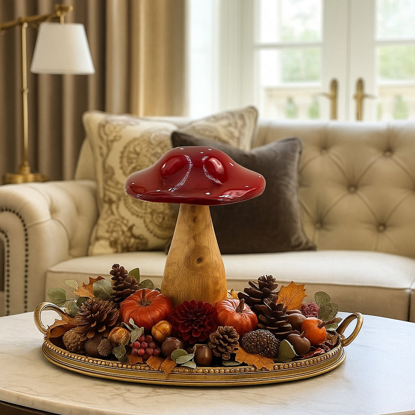 Ciupercă decorativă din lemn cu pălărie roșie așezată pe o tavă de bronz, decorată de toamnă. Tava se află pe o măsuță cu blat de marmură, în fața unei canapele