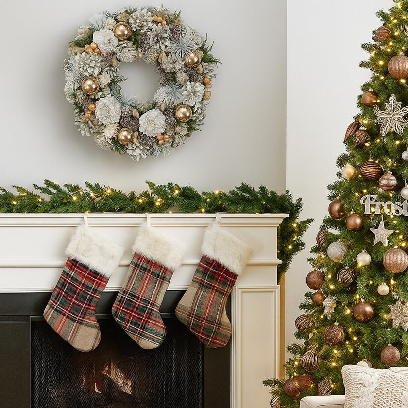 Coroniță de Crăciun cu conuri ninse și globuri aurii, agățată pe un perete alb, deasupra unui șemineu alb decorat de Caăciun
