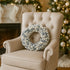 Coroniță de Crăciun cu globuri argintii și albe, așezată pe un fotoliu luxos, bej, din textil