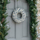 Coroniță de Crăciun cu globuri argintii și albe, agățată pe o ușă gri de intrare, decorată de Crăciun