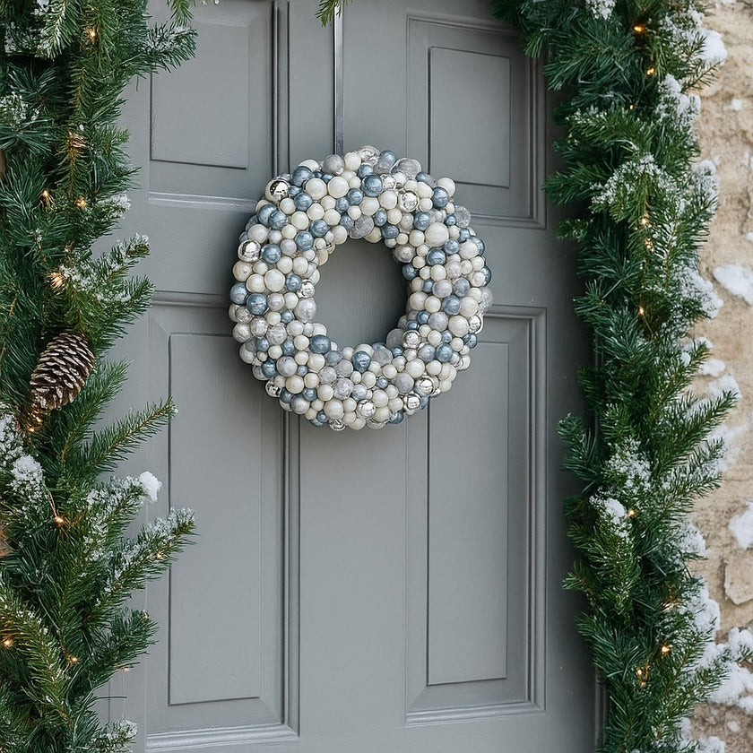 Coroniță de Crăciun cu globuri argintii și albe, agățată pe o ușă gri de intrare, decorată de Crăciun