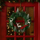 Coroniță de Crăciun, verde cu brazi ninși și reni agățată pe o ușă de intrare roșie, din lemn și sticlă, decorată de Crăciun