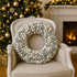 Coroniță de Crăciun cu globuri argintii și albe, așezată pe  un scaun luxos, din lemn si textil, în fața unui șemineu