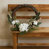 Coroniță Advent rustică cu flori albe și frunze verzi sprijinită pe o bancă rustica, de lemn