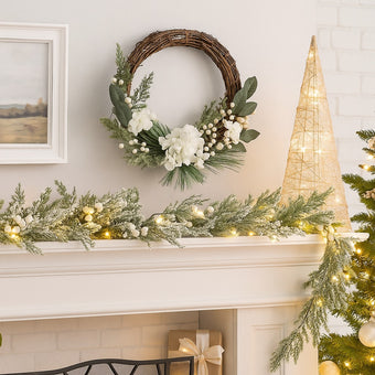 Coroniță Advent rustică cu flori albe și frunze verzi agățată deasupra unui șemineu alb, decorat de Crăciun