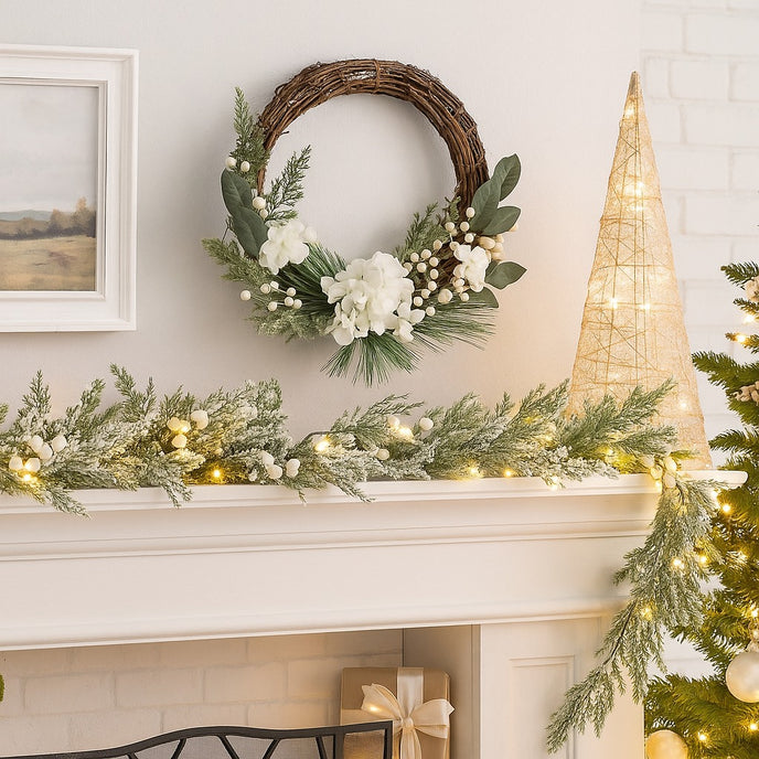 Coroniță Advent rustică cu flori albe și frunze verzi agățată deasupra unui șemineu alb, decorat de Crăciun