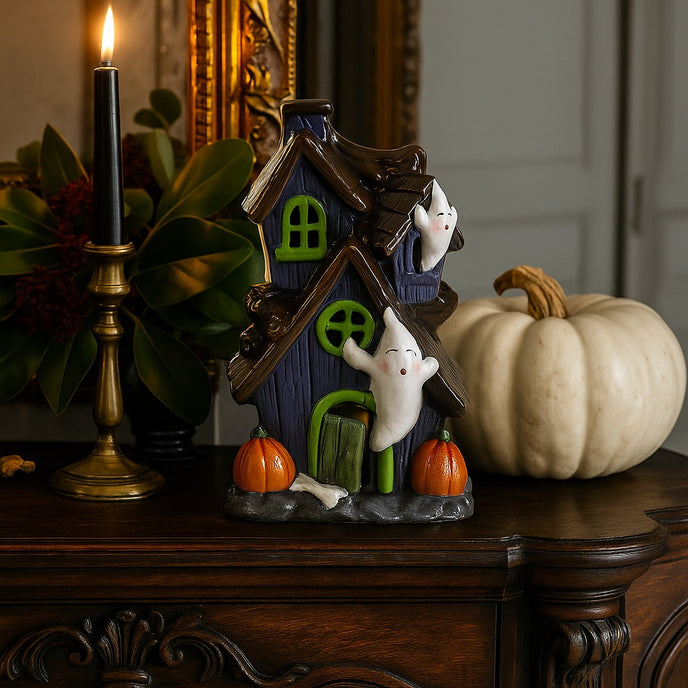 Decorațiune de Halloween în formă de casă bântuită cu fantome, dovleci și lumină led, așezată pe un bufet din lemn, decorat de Halloween