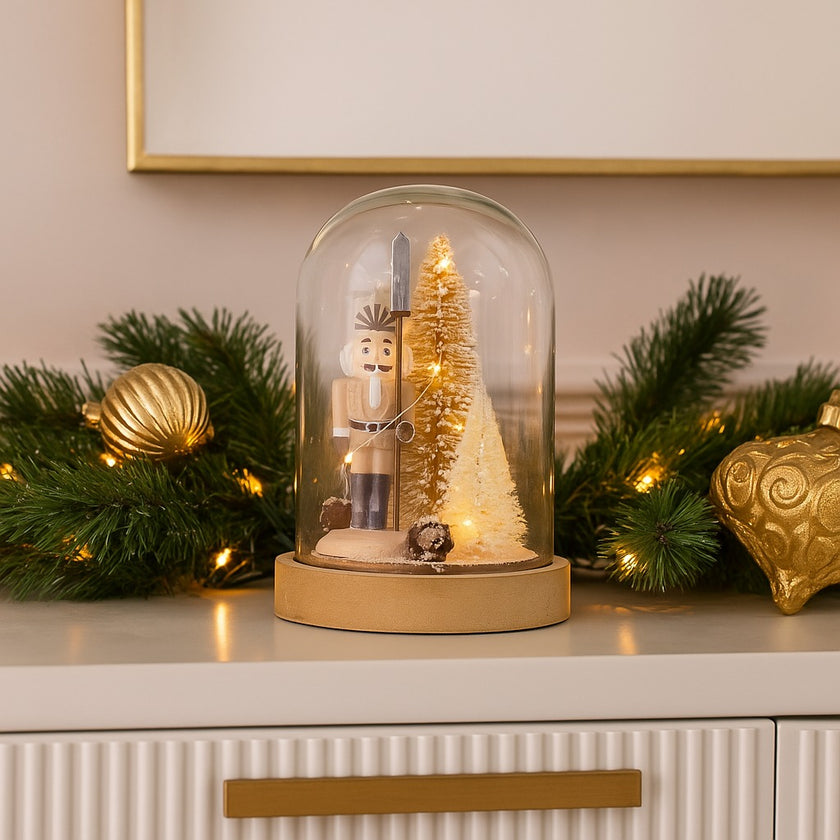 Decorațiune spărgător de nuci în clopot de sticlă cu lumini led așezată pe pe un bufet alb, decorat de Crăciun