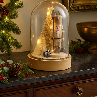 Decorațiune spărgător de nuci în clopot de sticlă cu lumini led așezată pe un bufet cu blat de piatră neagră, deocrat de Crăciun