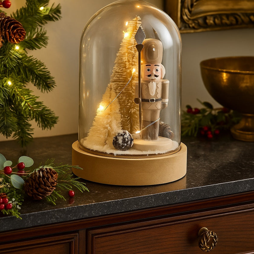 Decorațiune spărgător de nuci în clopot de sticlă cu lumini led așezată pe un bufet cu blat de piatră neagră, deocrat de Crăciun