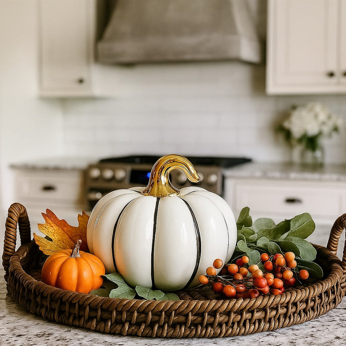 Dovleac decorativ alb cu codiță aurie pentru toamnă așezat pe un blat in bucătărie, pe o tavă de răchită decorată de tomană