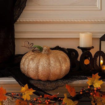 Dovleac decorativ auriu cu sclipici așezat pe o manta de șemineu, decorată de Halloween