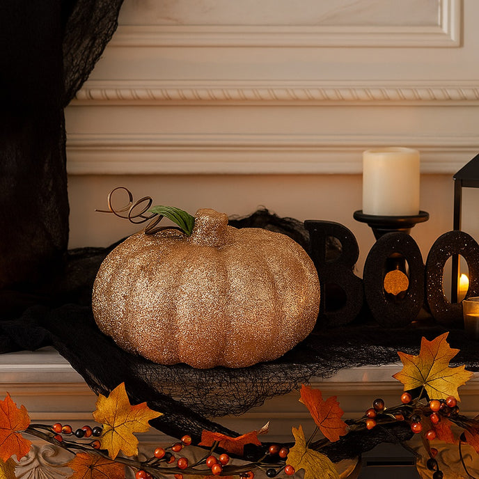 Dovleac decorativ auriu cu sclipici așezat pe o manta de șemineu, decorată de Halloween