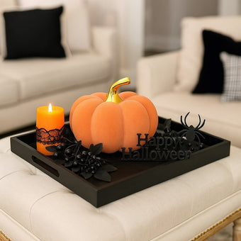 Dovleac decorativ din catifea, portocaliu cu auriu, așezat pe o tavă neagră din lemn, decorată de Halloween. Tava este așezată p eun taburete din textil