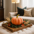 Dovleac decorativ din catifea, portocaliu cu auriu, așezat pe o tavă maro, din lemn. decorată de toamnă. Tava este p eun taburete tip otoman