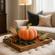 Dovleac decorativ din catifea, portocaliu cu auriu, așezat pe o tavă maro, din lemn. decorată de toamnă. Tava este p eun taburete tip otoman
