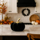 Dovleac decorativ negru, din catifea, cu codiță aurie, așezat pe un blat alb de bucătărie, decorată de toamnă