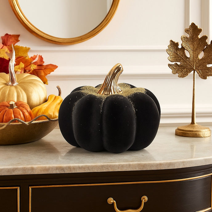 Dovleac decorativ negru, din catifea, cu codiță aurie, așezat pe un bufet cu blat de marmura, decorat de toamnă