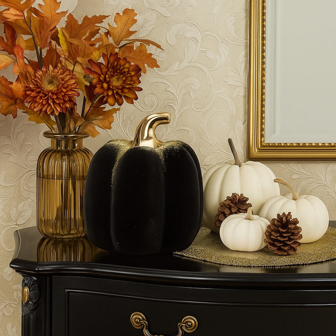 Dovleac decorativ negru, din catifea, cu codiță aurie așezat pe un bufet luxos, din lemn negru, decorat de toamnă