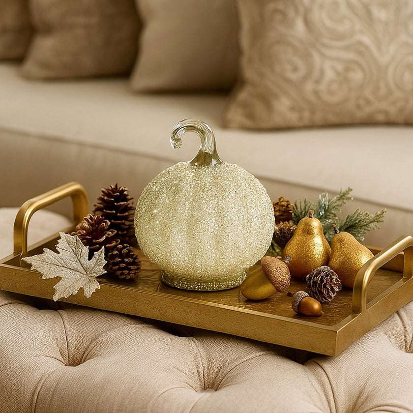 Dovleac decorativ din sticlă, de culoare albă și acoperit cu paiete, așezat pe o tavă aurie, deocrată de toamnă