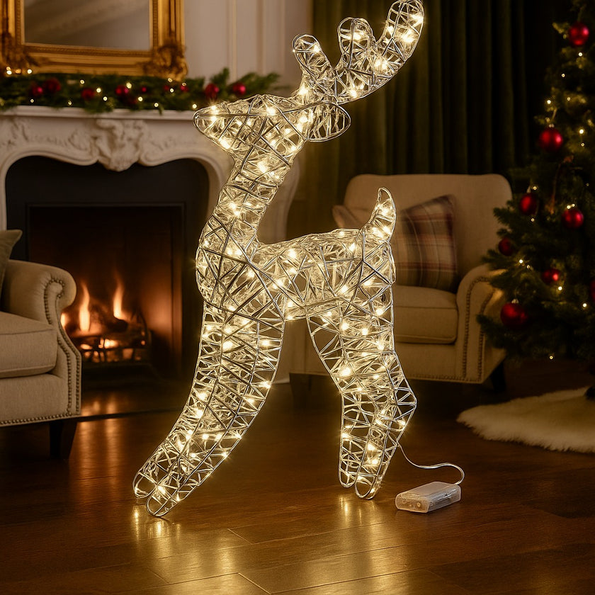 Figurină 3D în formă de ren cu lumini LED așezată într-un living decorat de Crăciun, în fața unui șemineu