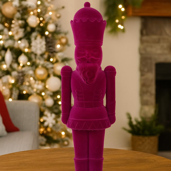 Figurină spărgător de nuci mov catifelat așezată pe o masă, într-un living decorat de Crăciun