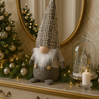 Gnom decorativ de Crăciun cu pălărie lungă gri așezat pe un bufet de lemn alb cu auriu și blat der marmura, decorat de Crăciun