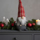 Gnom decorativ de Crăciun cu pălărie lungă roșie așezat pe un bufet de lemn, gri decorat de Crăciun