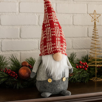 Gnom decorativ de Crăciun cu pălărie lungă roșie așezat pe un bufet de lemn maro, decorat de Crăciun
