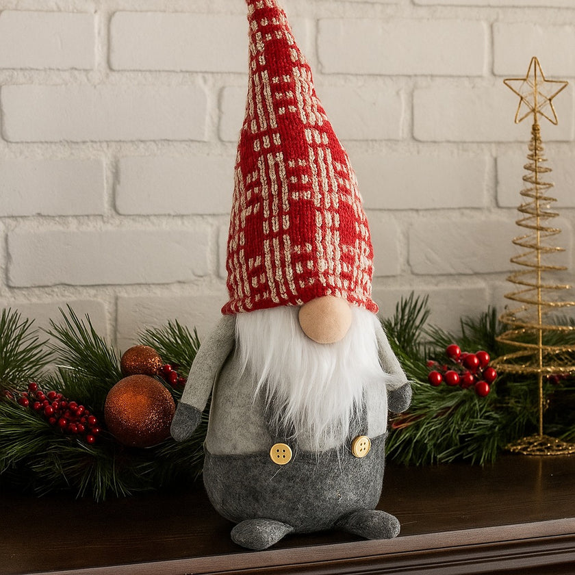 Gnom decorativ de Crăciun cu pălărie lungă roșie așezat pe un bufet de lemn maro, decorat de Crăciun