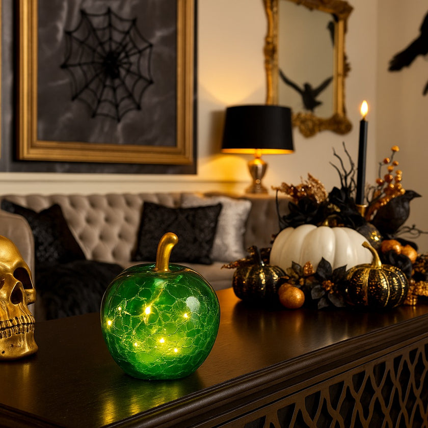 Măr decorativ din sticlă, de culoare verde, cu lumină led, așezat pe un bufet din lemn, decorat de Halloween