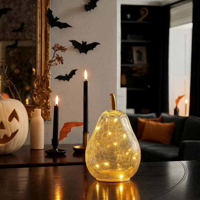Pară decorativă din sticlă transparentă, cu lumină led, așezată pe un blat de masă din lemn, decorat de Halloween