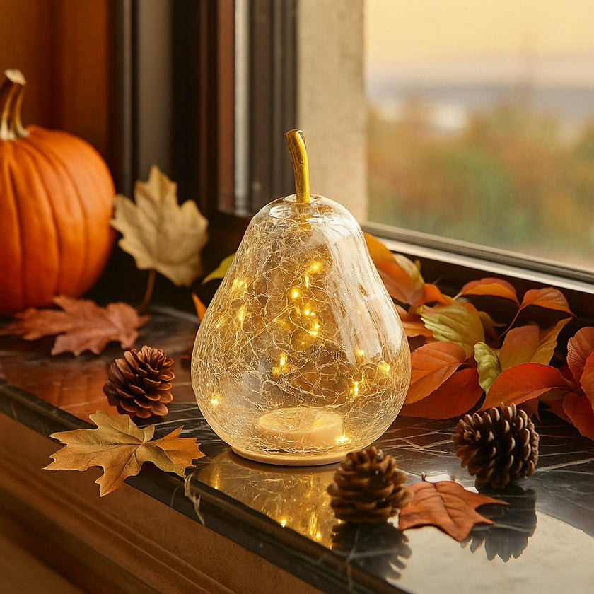 Pară decorativă din sticlă transparentă, cu lumină led, așezată pe un pervaz din marmură neagră, decorat de toamnă