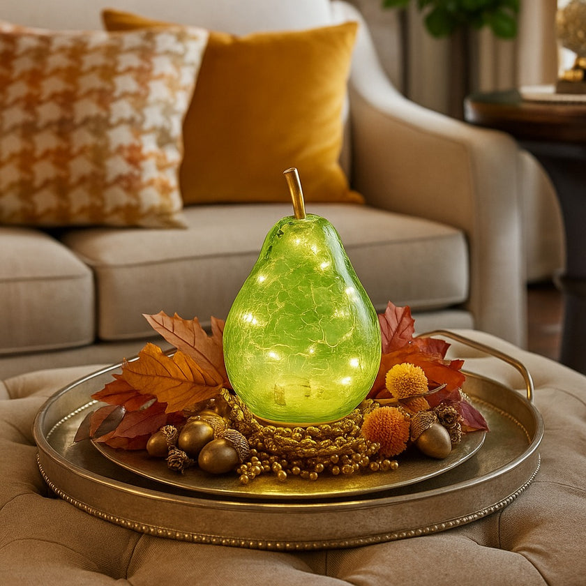 Pară decorativă din sticlă, de culoare verde, cu lumină led, așezată pe aurie, decorată de toamnă