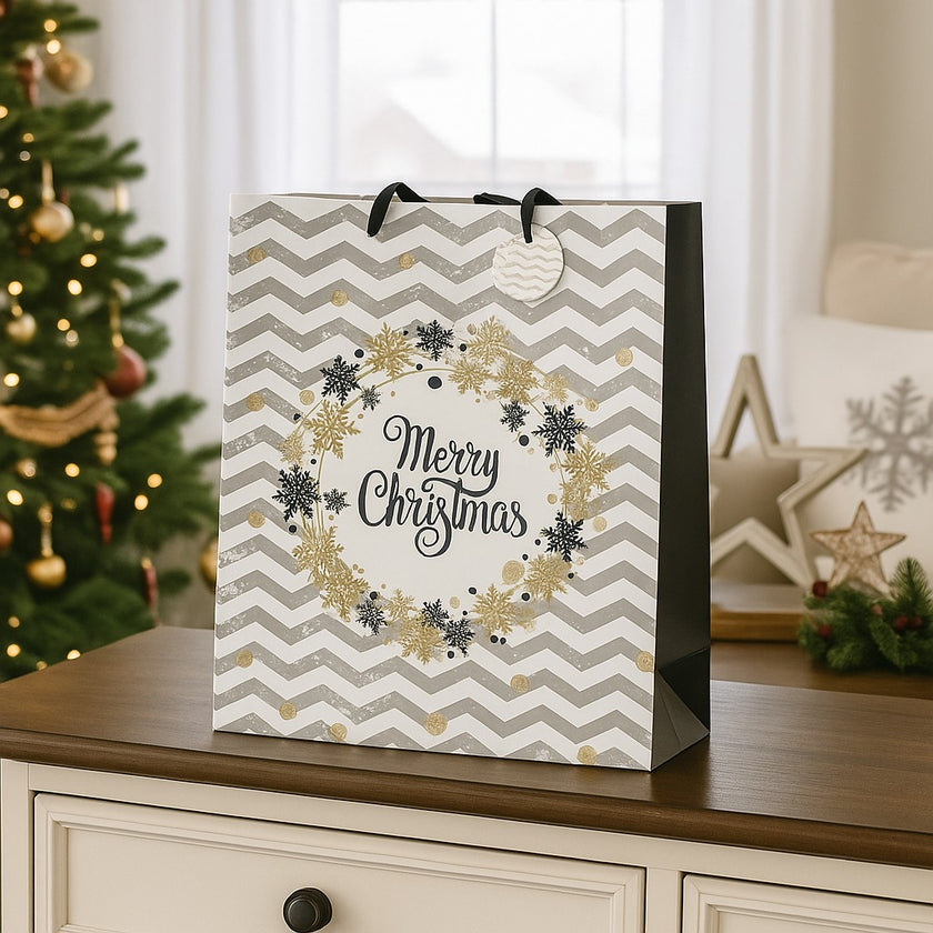 Pungă cadou de Crăciun, cu model zig-zag în alb și gri, cu fulgi aurii, asezată pe unbufet alb și bșat maro, decorat de Crăciun