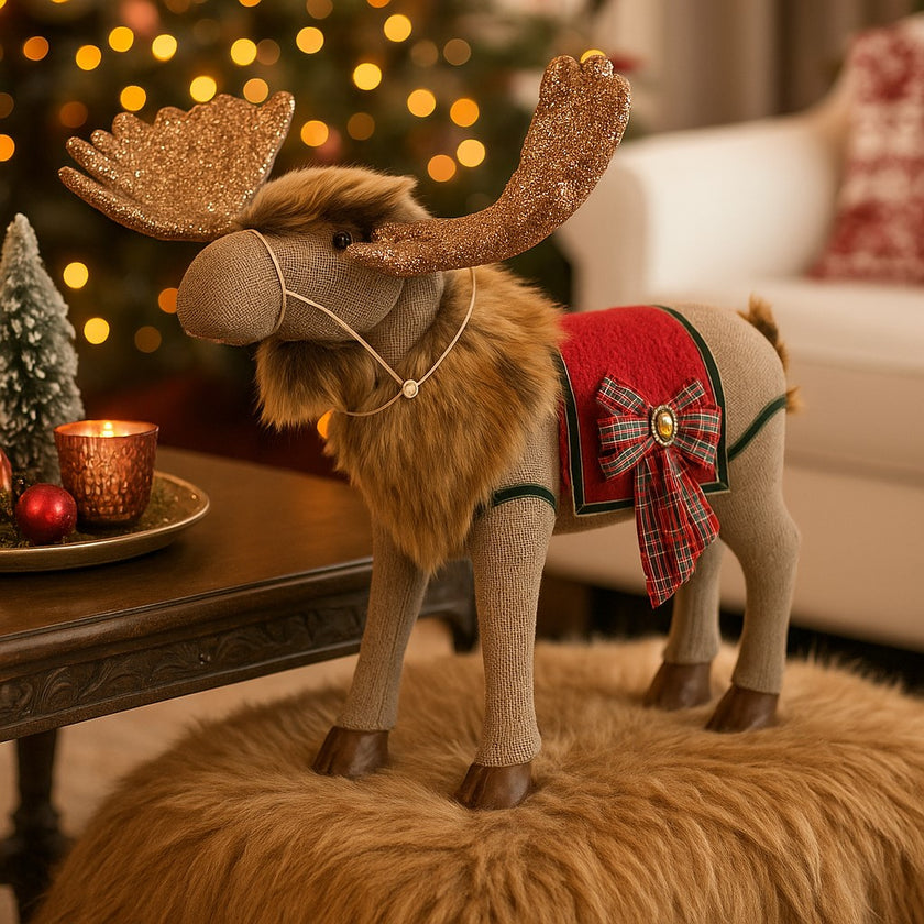 Ren decorativ de Crăciun, din material textil, cu coarne aurii și sclipitoare, așezat pe un taburete de blană maro, lângă o masă de lemn maro, deocrată de Crăciun