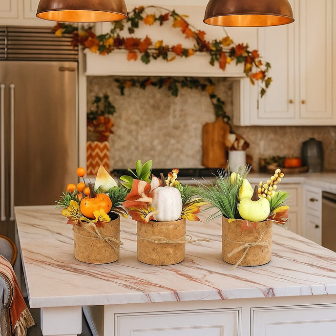 Set 3 aranjamente dovlecei de toamnă în ghiveci de plută, așezate pe o insulă cu blat alb, în bucătărie decorată de toamnă