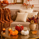 Set de 3 dovleci decorative, textile, de culoare portocaliu roșu și alb, așezați pe o masă aurie, cu blat din sticlă, decorată de toamnă