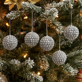 Set globuri argintii de Crăciun cu cristale, agățate pe un brad nins, decorat de Crăciun