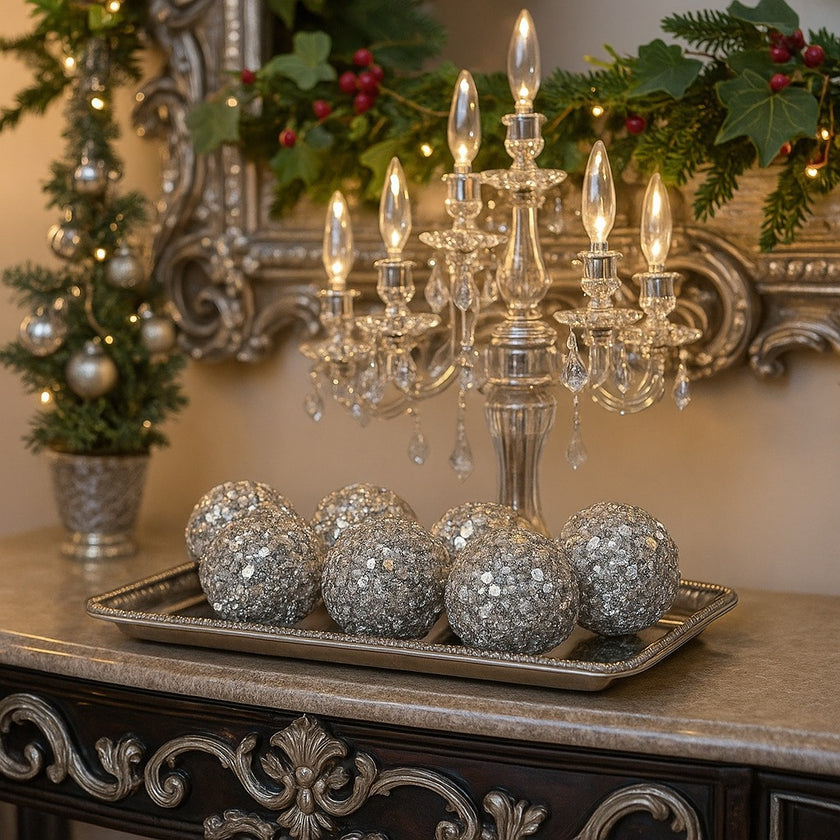 Set globuri argintii de Crăciun cu cristale, așezate pe o tava metalică, argintie. Tava este așezată pe o comodă decorată de Crăciun