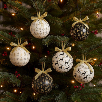 Set globuri de Crăciun in culori de alb, negru și auriu agățate pe un brad verde, decorat de Crăciun