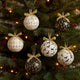 Set globuri de Crăciun in culori de alb, negru și auriu agățate pe un brad verde, decorat de Crăciun