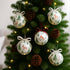 Set globuri de Crăciun cu imprimeuri de iarnă așezate pe un brad verde cu conuri maro