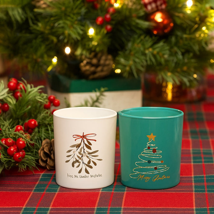 Set de două suporturi din sticlă, cu brad și vâsc, pentru lumânări decorative de Crăciun, așezate pe o masa festivă, decorată de Crăciun