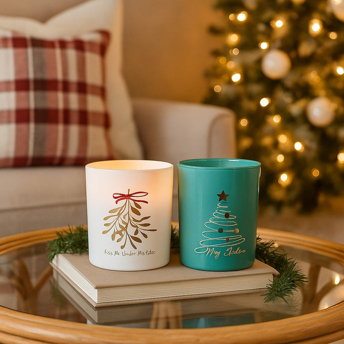 Set de două suporturi din sticlă, cu brad și vâsc, pentru lumânări decorative de Crăciun, așezate pe o carte ce se află masă rotundă din sticlă