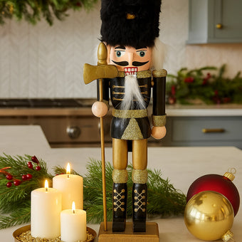 Spărgător de nuci cu căciulă de blană, negru cu auriu așezat pe un blat alb de bucătărie, decorat de Crăciun