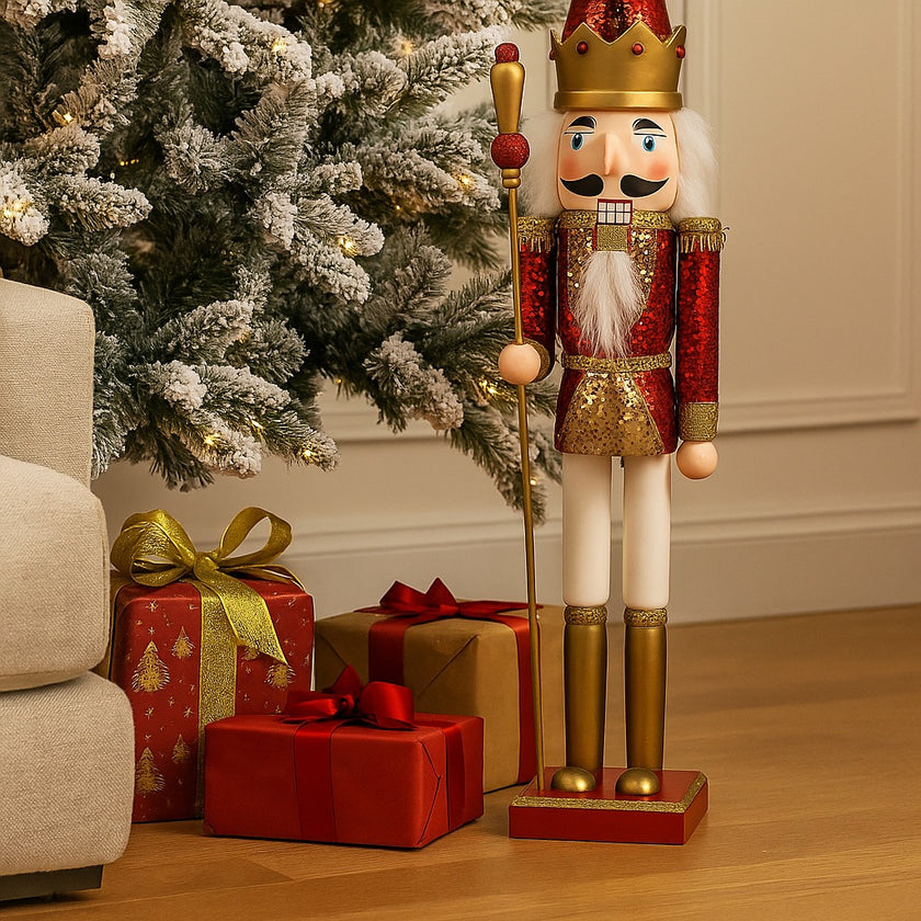 Spărgător de nuci Crăciun roșu și auriu așezat lângă un brad nins și cadouri împachetate de Crăciun