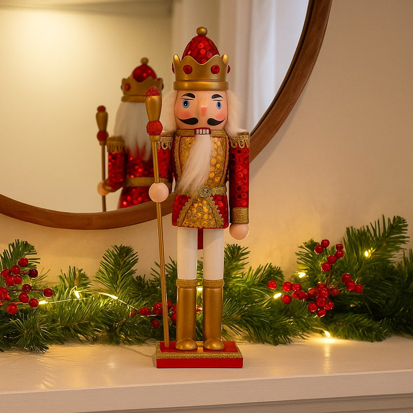 Spărgător de nuci roșu și auriu așezat pe o manta de șemineu albă, decorată de Crăciun